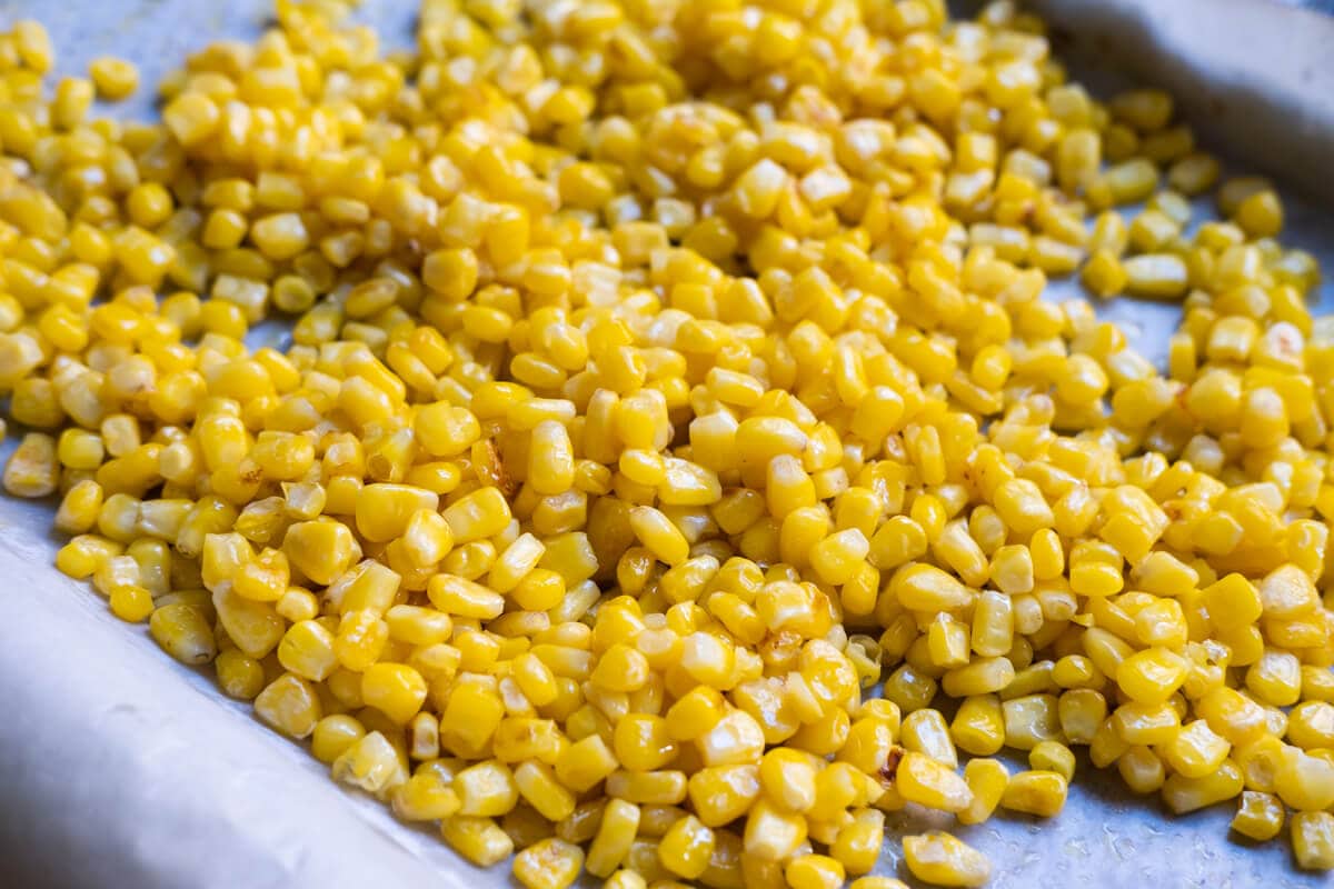 A single layer of corn arranged on the oven tray lined with baking paper. 
