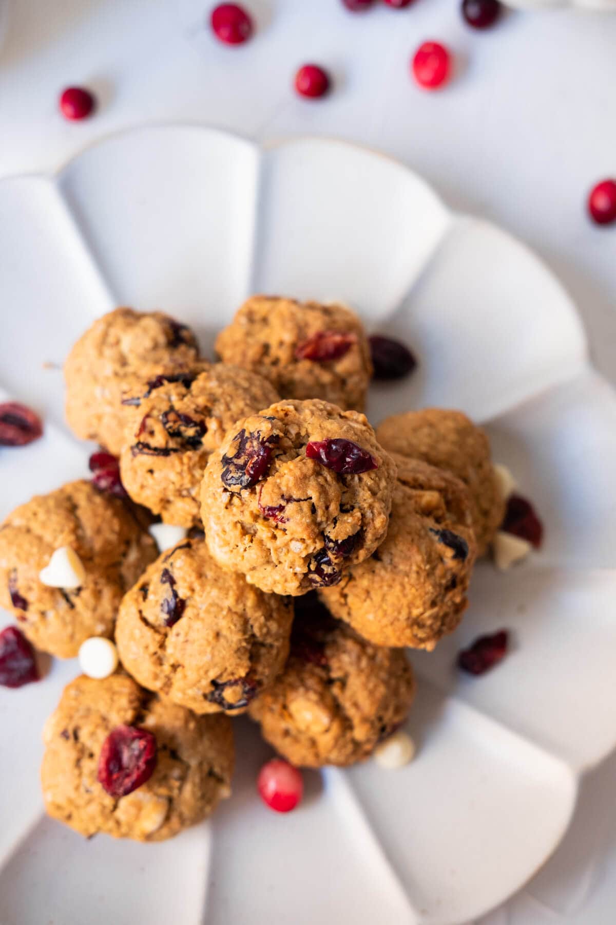 Crispy oatmeal chocolate cranberry cookies on a white plate with fresh cranberries on the side.