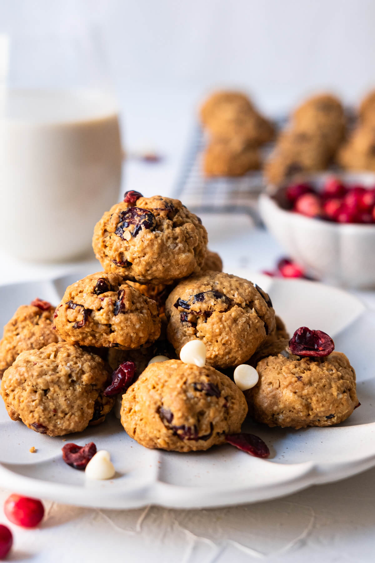 Oatmeal chocolate cranberry cookies on a plate with a cup of milk and a bowl of fresh cranberries placed aside.. 
