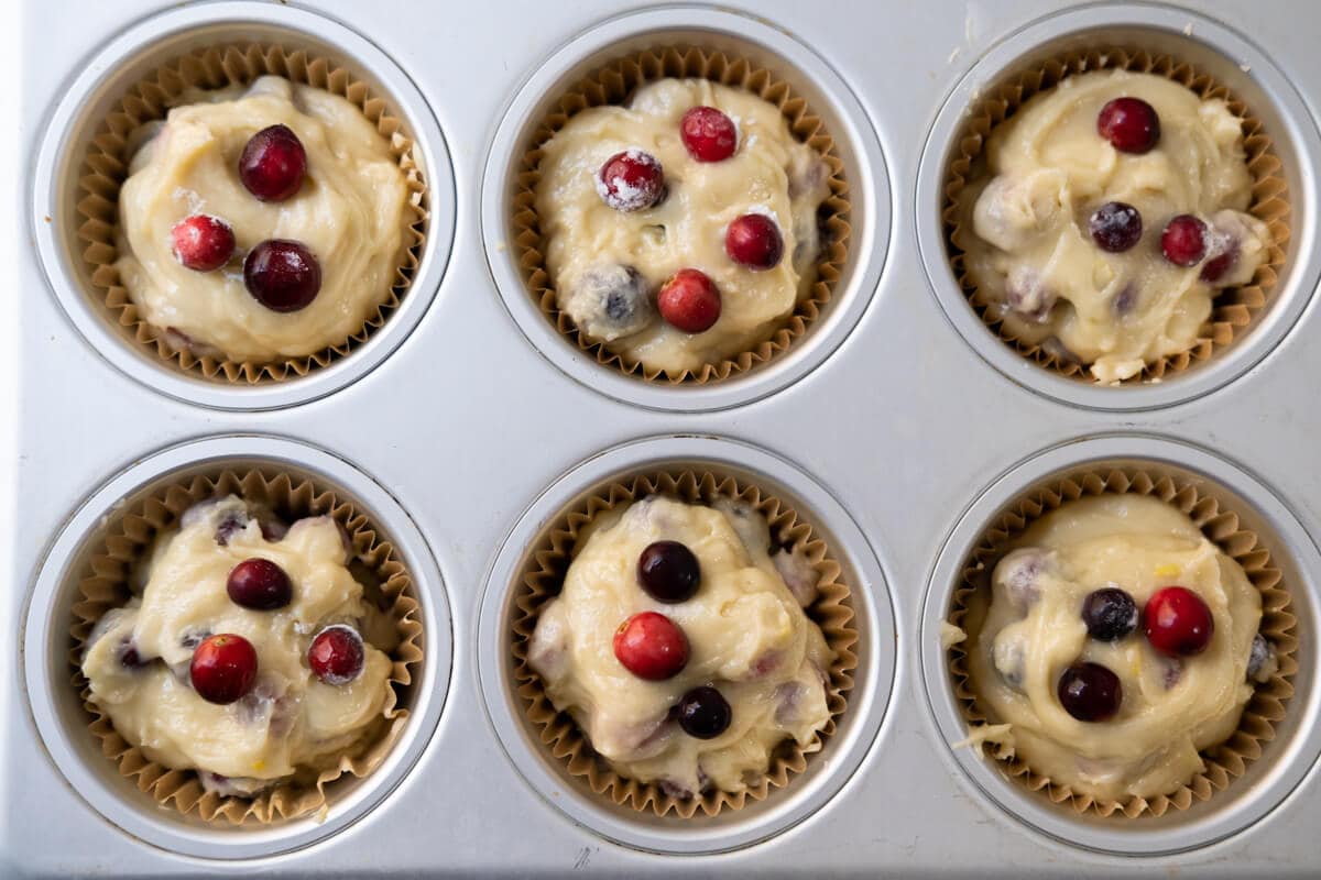 Batter with cranberries on top in  a muffin tin. 