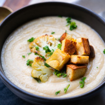 Creamy cauliflower soup with croutons, roasted cauliflower florets and chopped parsley on top.