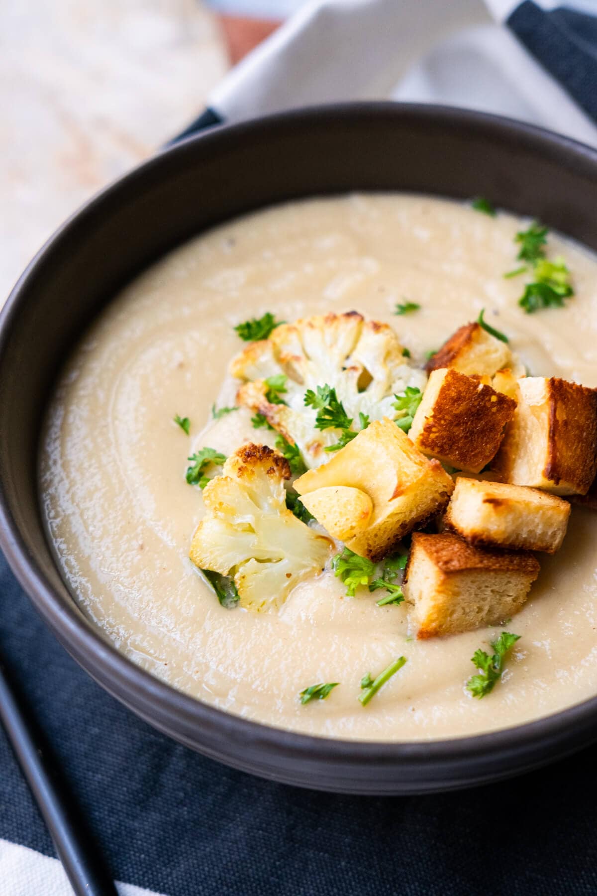 Silky smooth creamy cauliflower soup in a bowl with two florets and croutons on top. 
