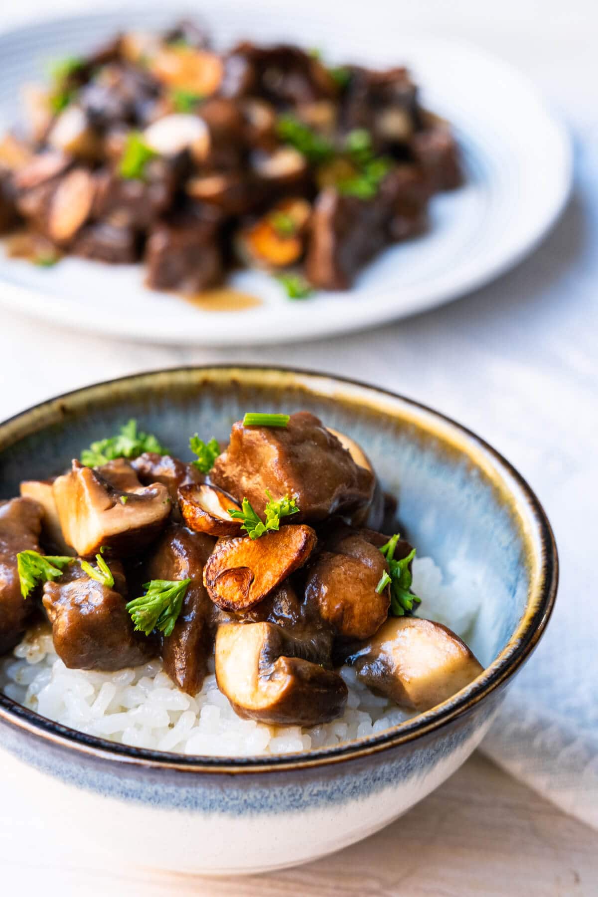 Beef and mushroom stir-fry in a plate and also served over the white rice in a small bowl. 
