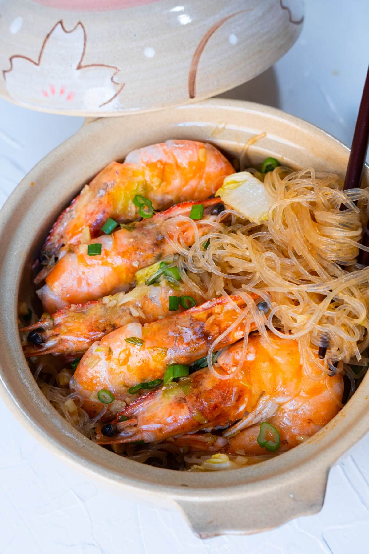 Shrimp and glass noodles in a clay pot with the lid on aside. 