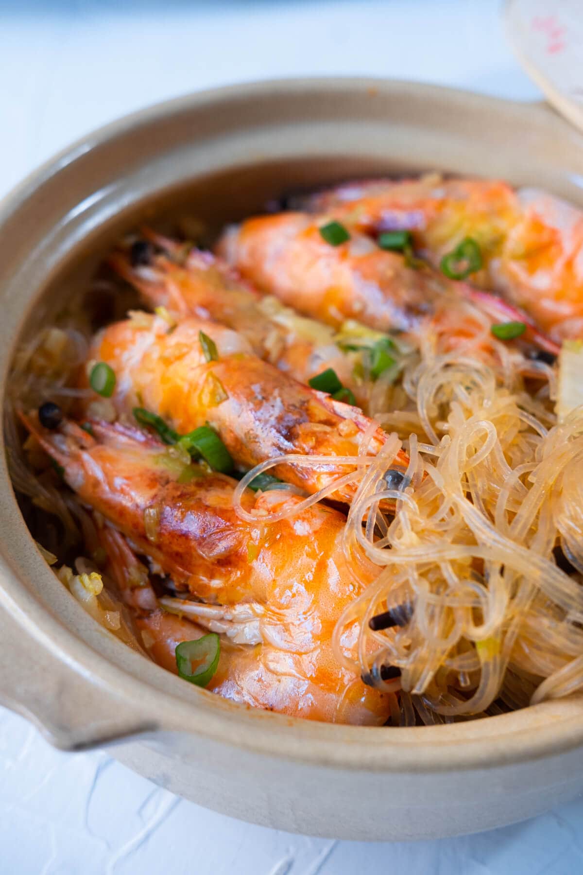 Shrimp and glass noodles in a clay pot with chopped green onion sprinkled on top. 
