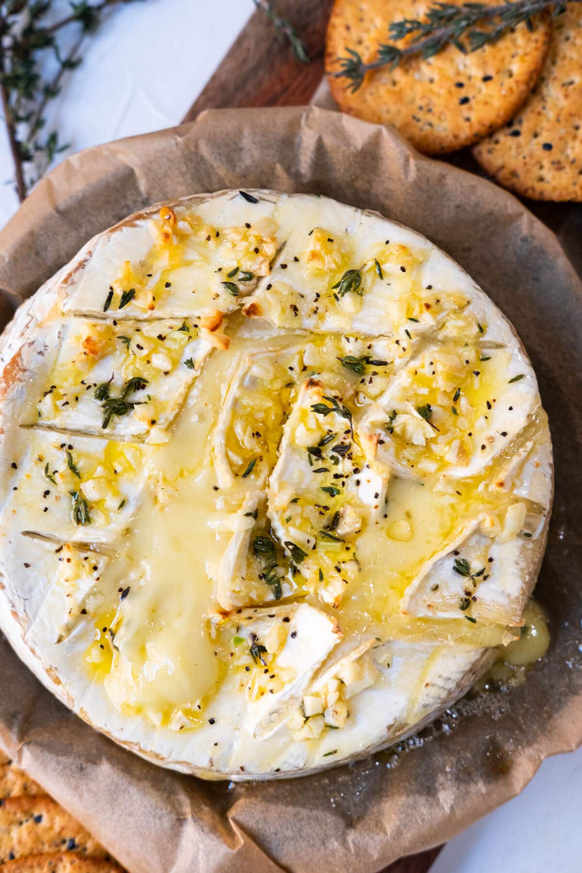 Garlic butter baked brie is served on a serving plate with whole-grain crackers aside. 