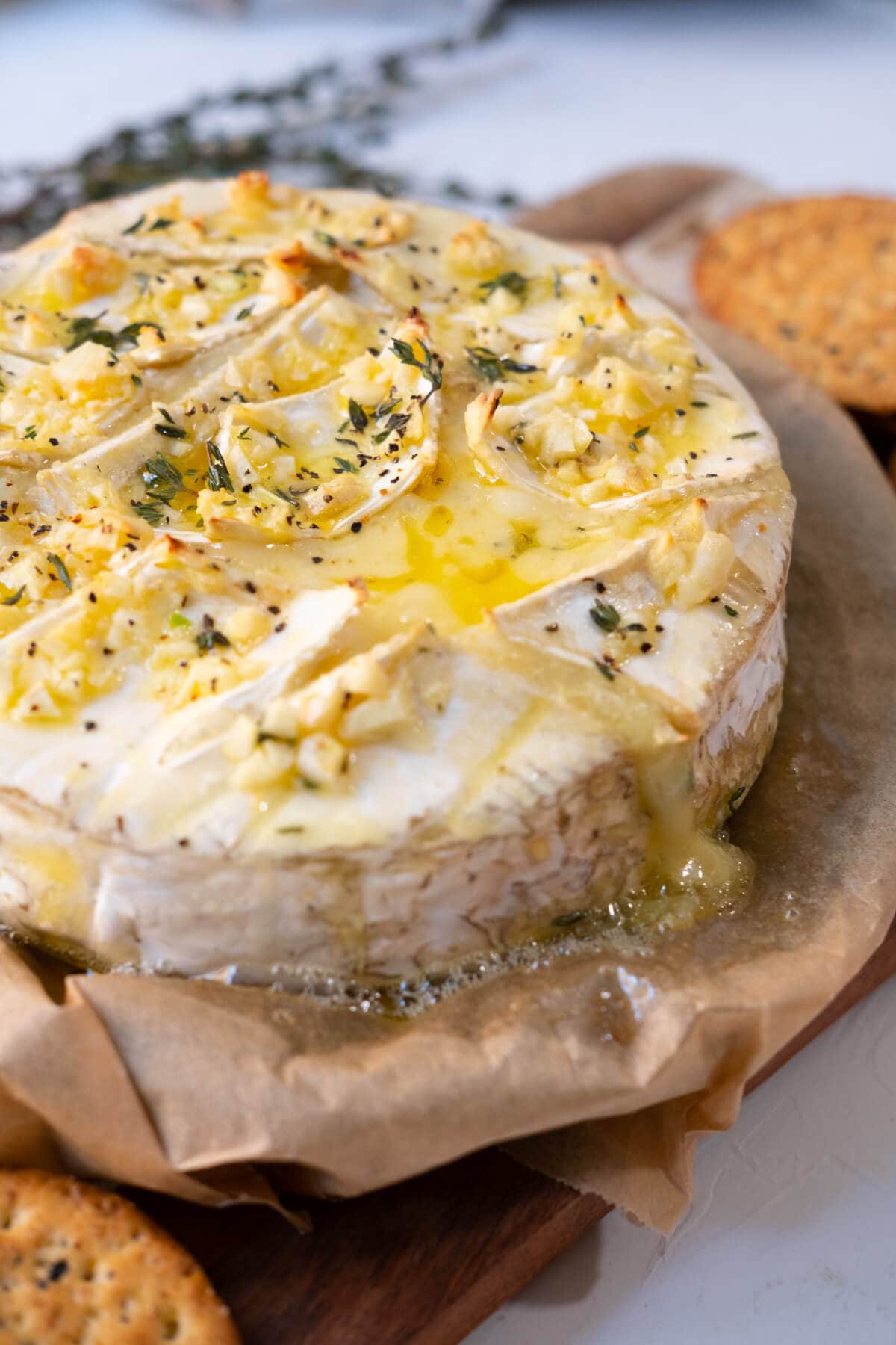 Baked brie topped with garlic and herbs and molten cheese dripping down from the edge.