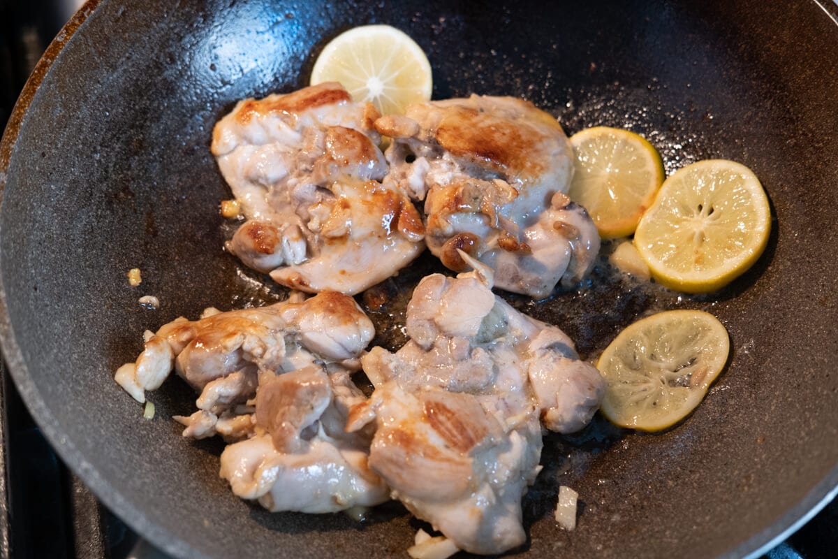 Chicken thighs and lemon cooked in a pan. 
