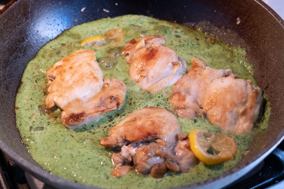 Chicken thighs and lemon cooked with Greek yogurt spinach sauce in a frying pan. 
