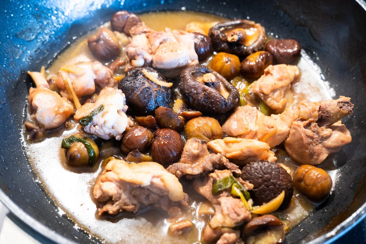 Shiitake mushrooms, chestnuts, and chicken simmering in pan. 