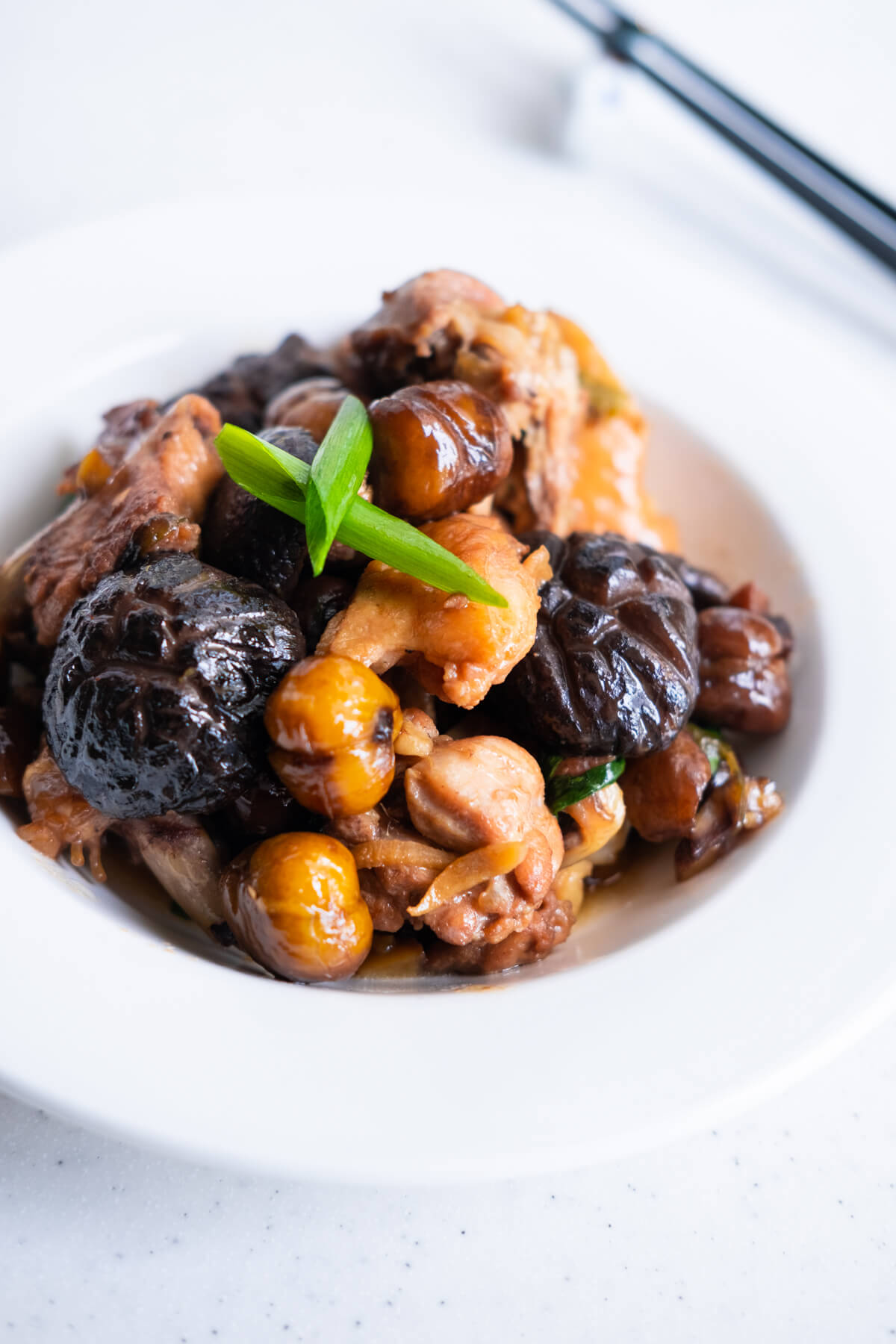 Brown cooked chicken, roasted chestnuts, and flavorful shiitake mushrooms served in a shallow bowl. 