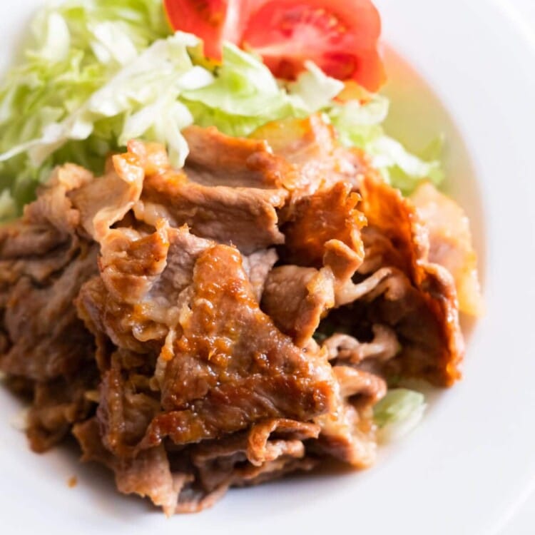 Flavorful Japanese ginger pork served in a plate with shredded lettuce and tomato.