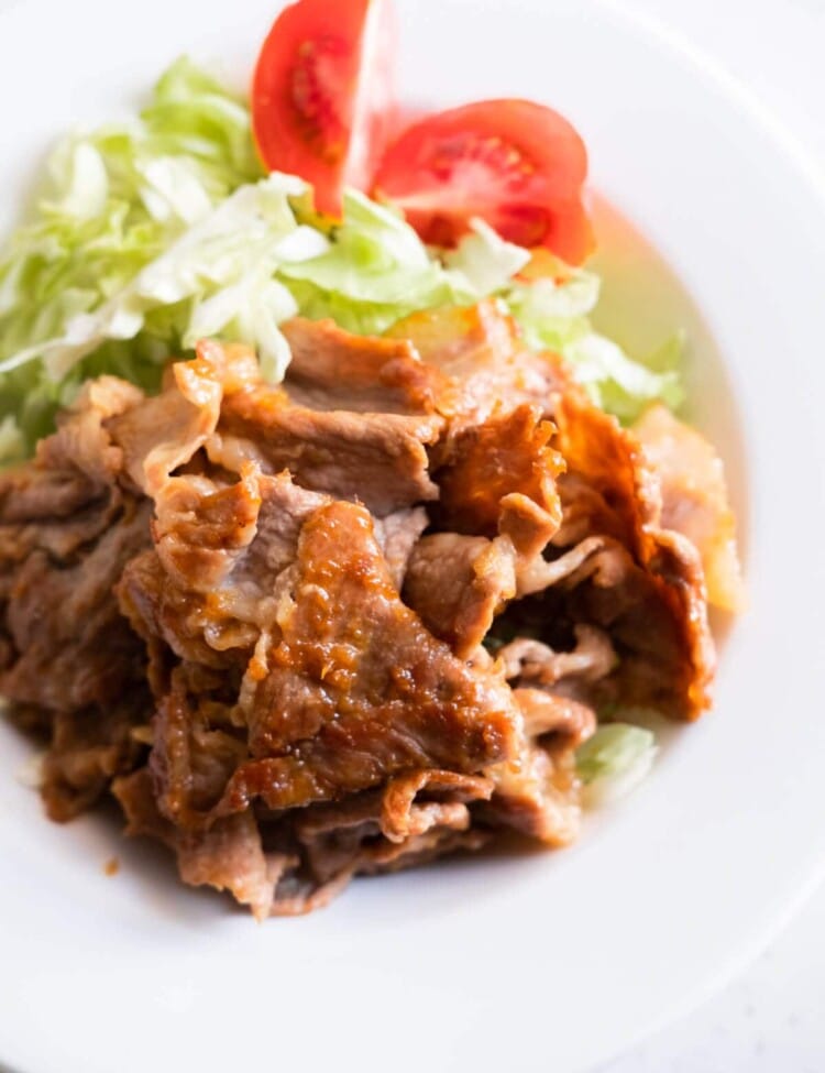Flavorful Japanese ginger pork served in a plate with shredded lettuce and tomato.