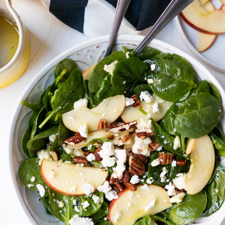 Spinach salad with three toppings, apple slices, chopped pecans and feta cheese crumbles.