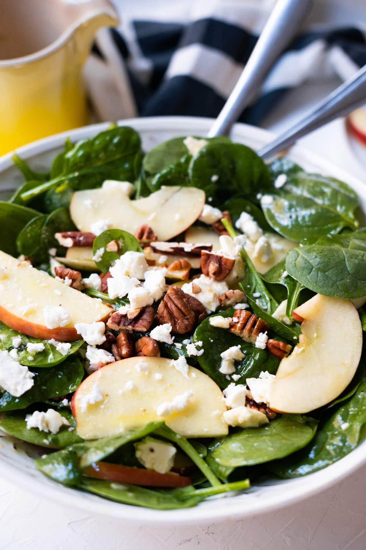 A bowl of spinach salad mixed baby spinach, chopped pecans, apple slices and feta cheese crumbles. 