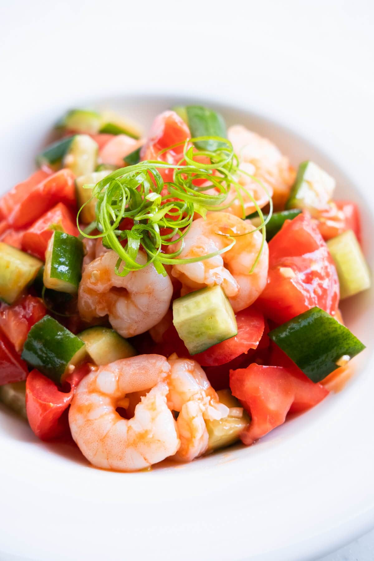 A bowl of shrimp, small pieces of tomatoes, and cucumber with scallion on top.