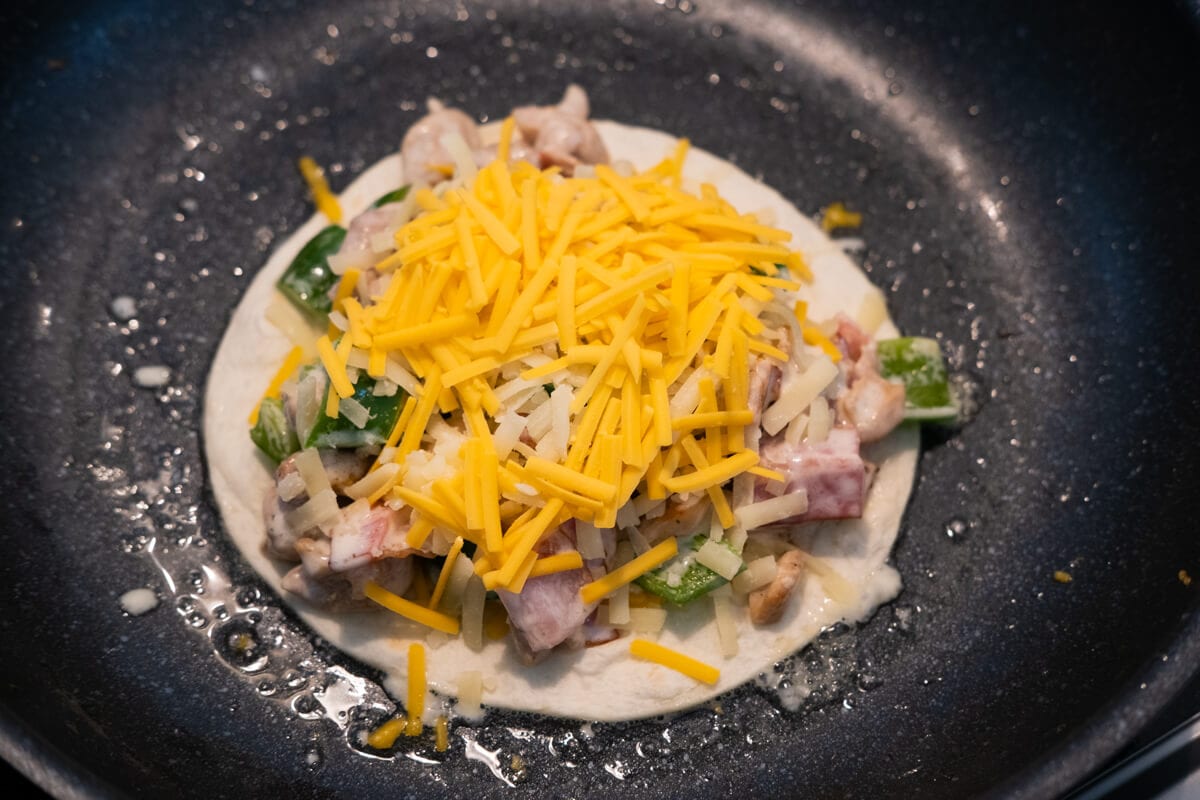 Assemble the quesadilla with chicken, bacon, green pepper, cheese and tortilla in a pan. 