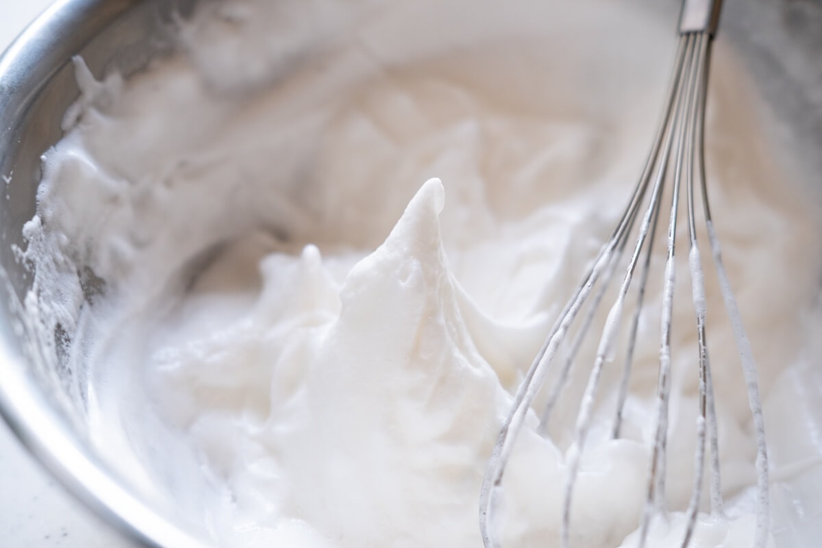 Egg whites being beat until stiff peaks with a whisk in a bowl. 
