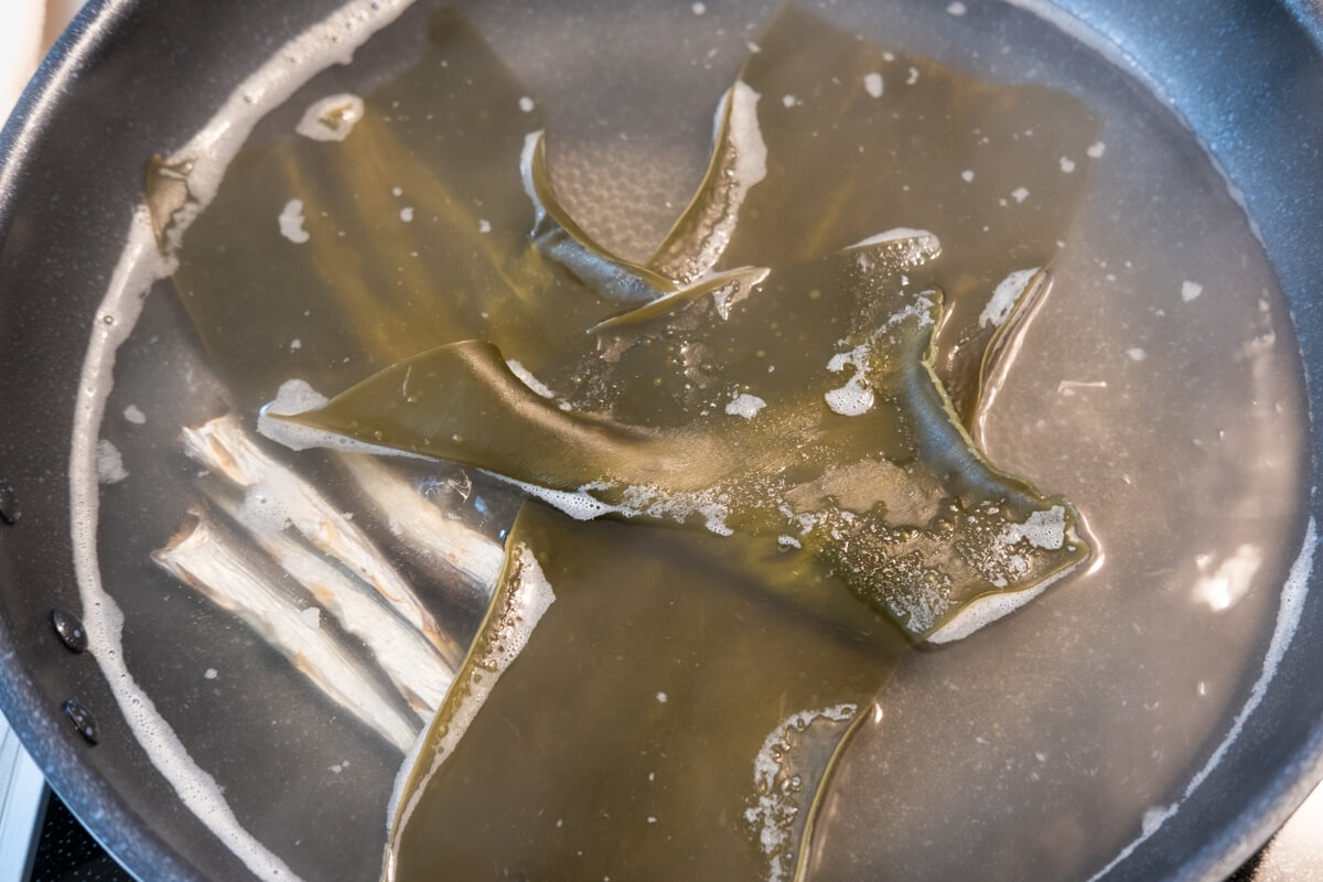 Two pieces of dried kelp boiling in water in a pot. 