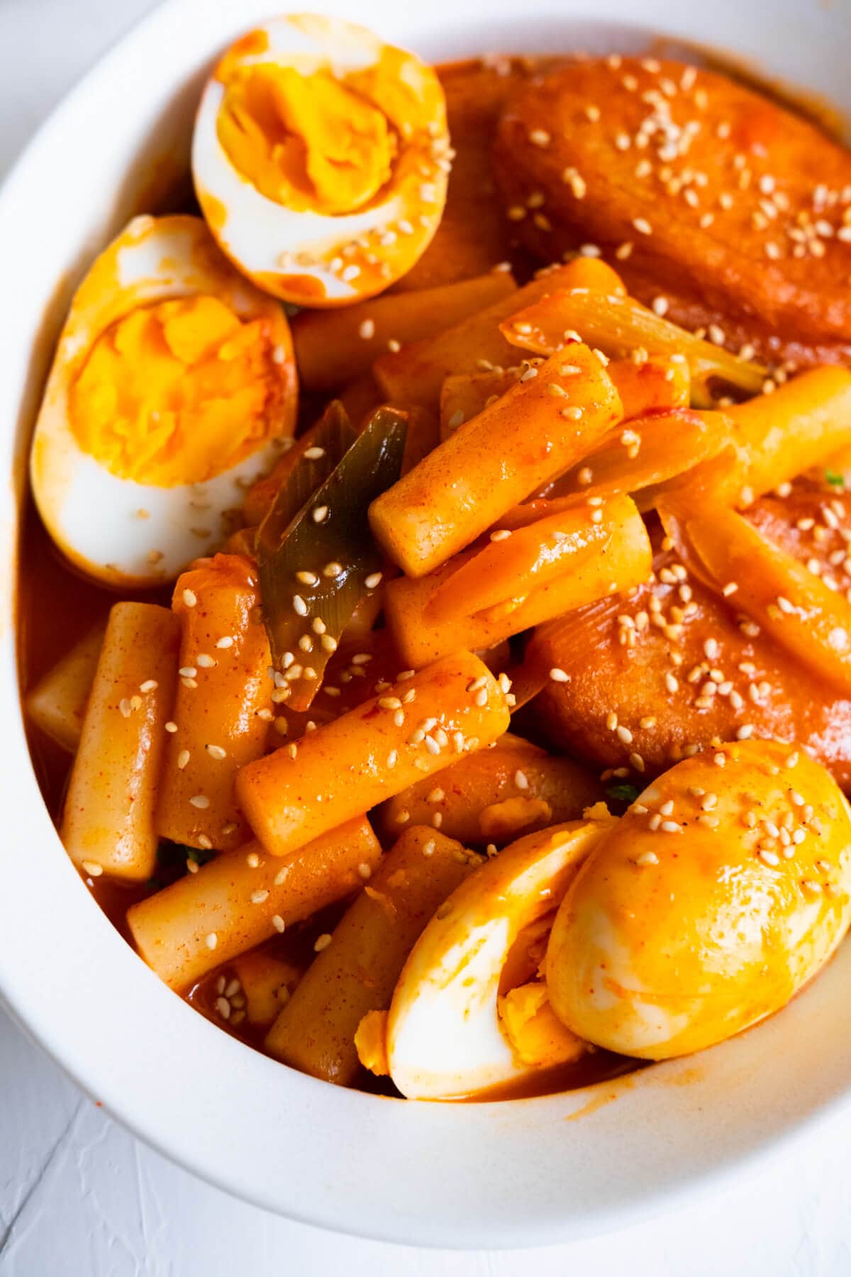 Spicy Korean rice cake, aka tteokbokki served in a shallow white plate with sesame seeds sprinkled on top. 
