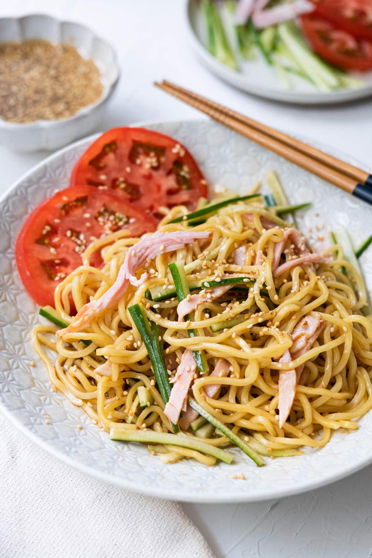 Simple and delicious noodle drizzled with homemade sesame dressing served on a white plate with tomato slices on the side. 
