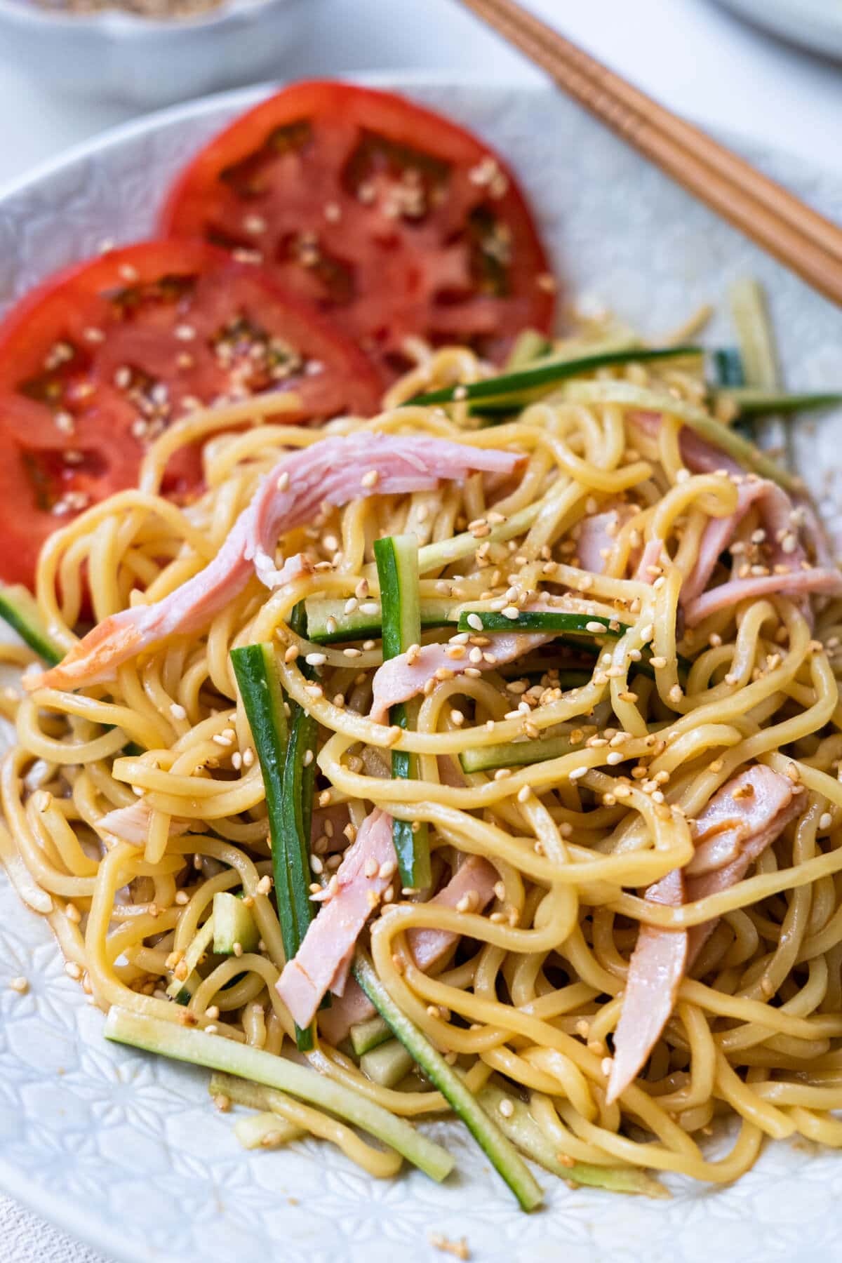 Close up shot of easy and quick noodle with tomato slices, julienne cucumber and ham slices dressed with sesame dressing served on a plate.