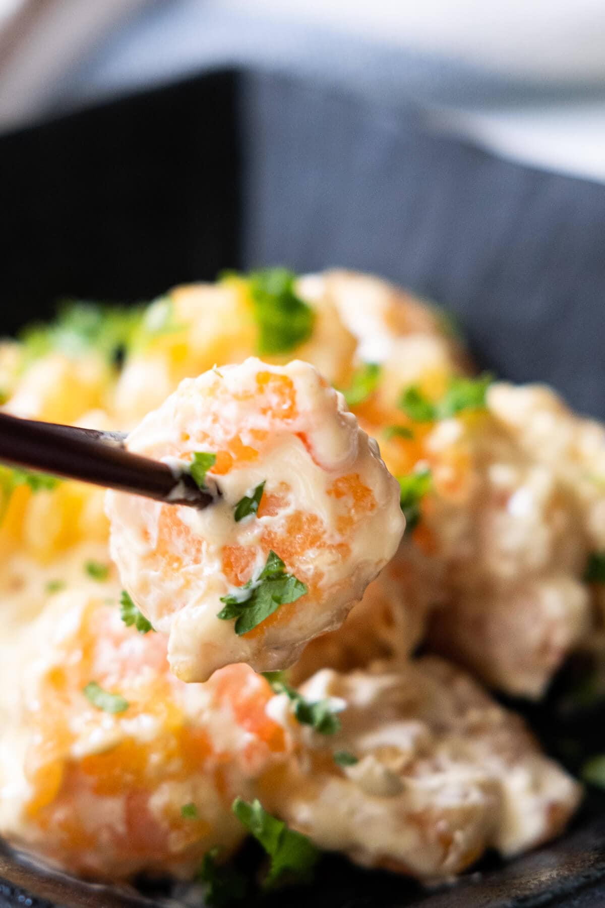 Close up shot of a tangy, flavorful  shrimp covered in mustard mayo sauce held by a chopstick. 
