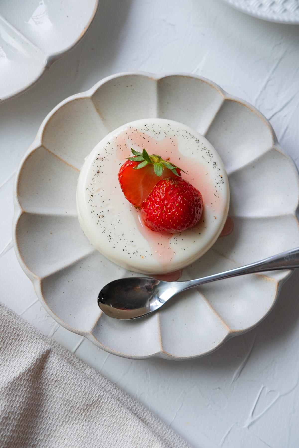 Panna cotta on a white shallow plate with a spoon aside. 