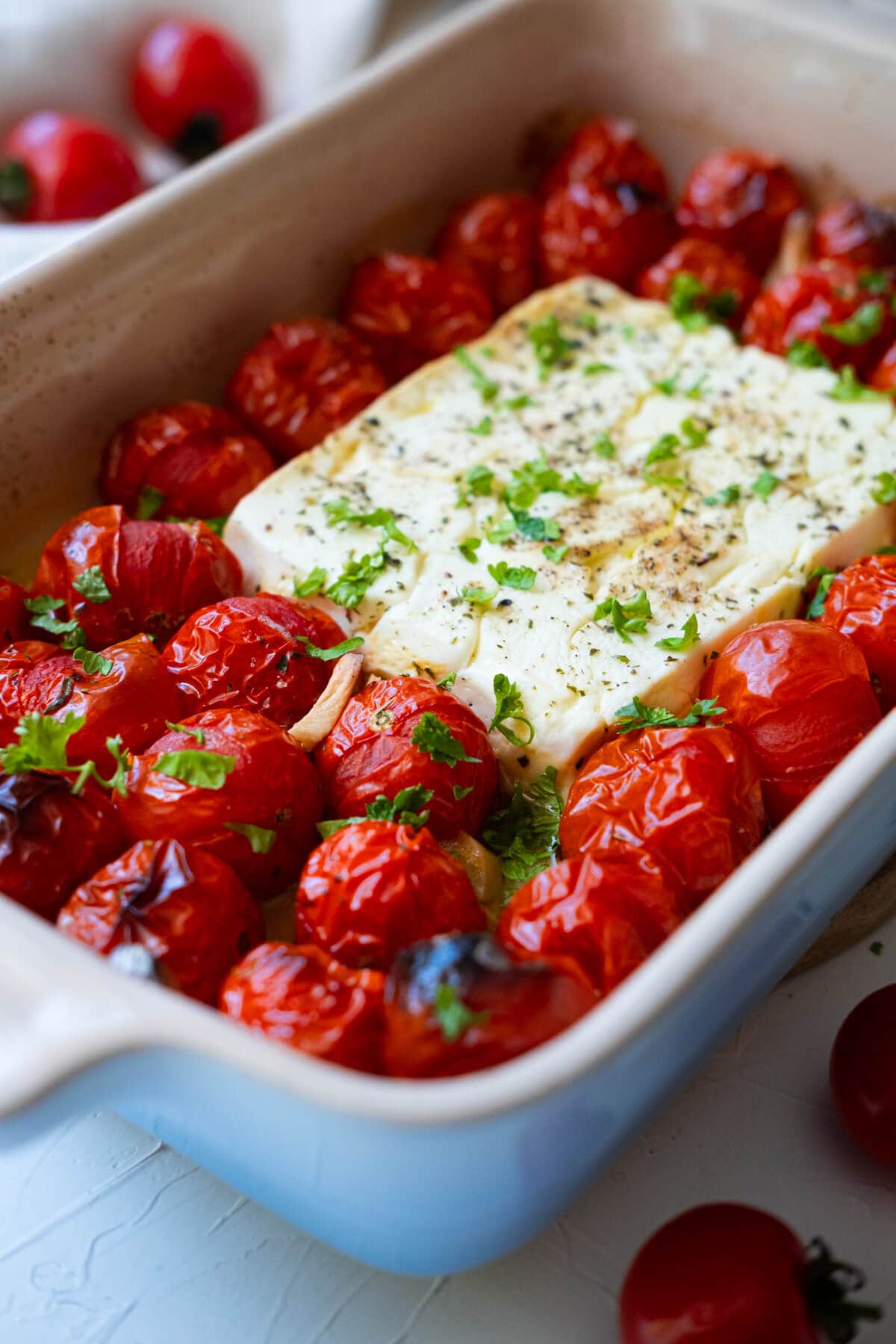 Baked tomato and feta with bursting tomato and golden brown feta cheese in the dish. 