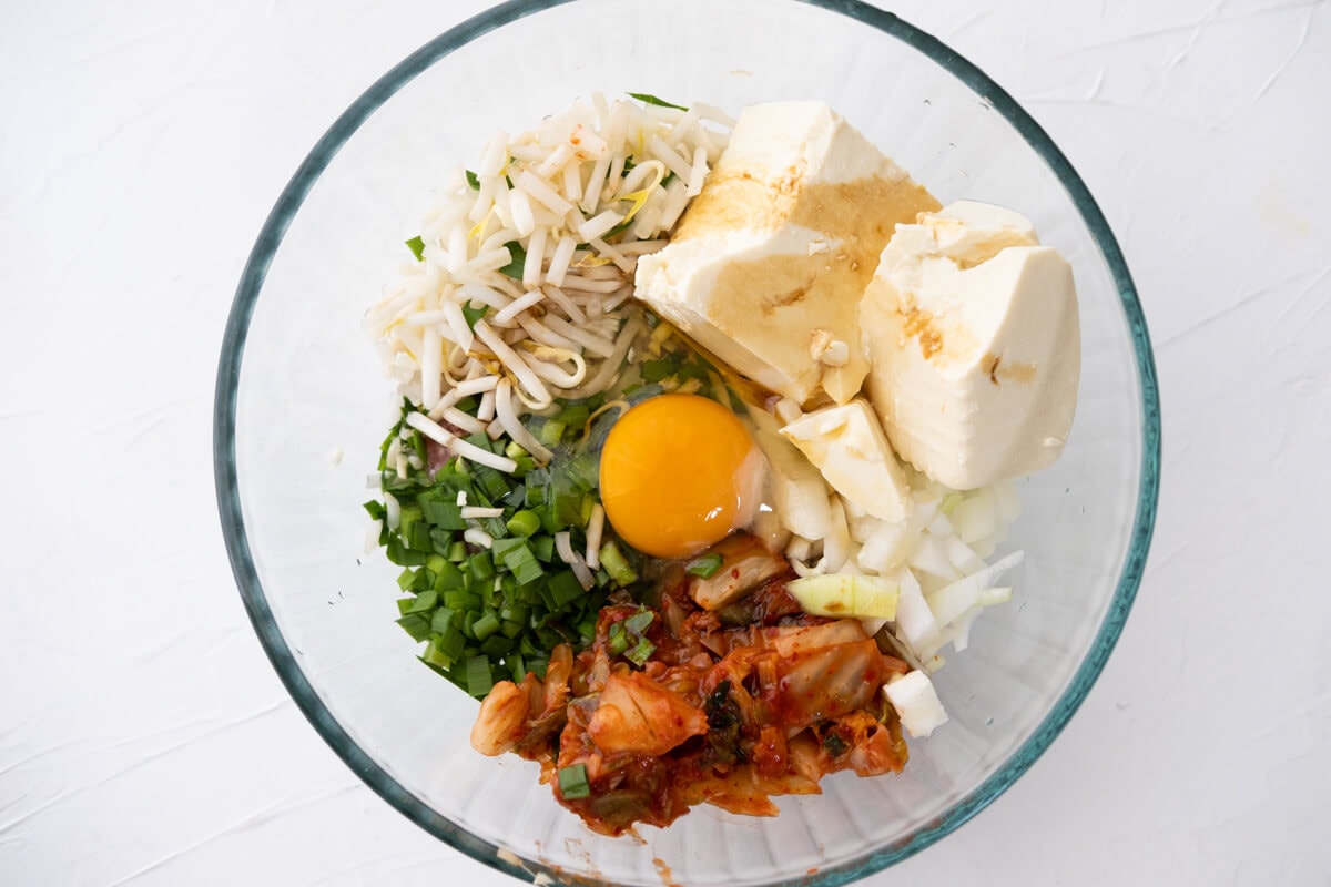 Kimchi, tofu, mung bean sprouts, onion, garlic chives, raw egg, garlic in a bowl.  