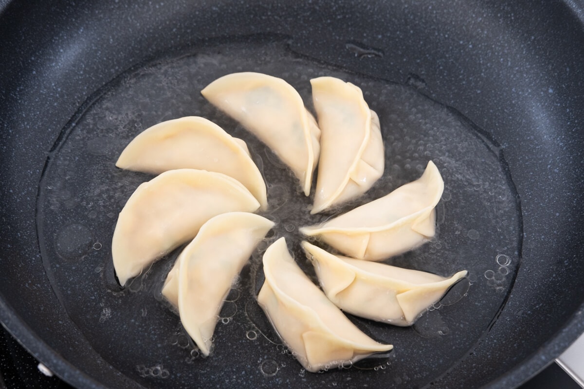 Mandu placed in a non-stick frying pan with oil surrounding it.  