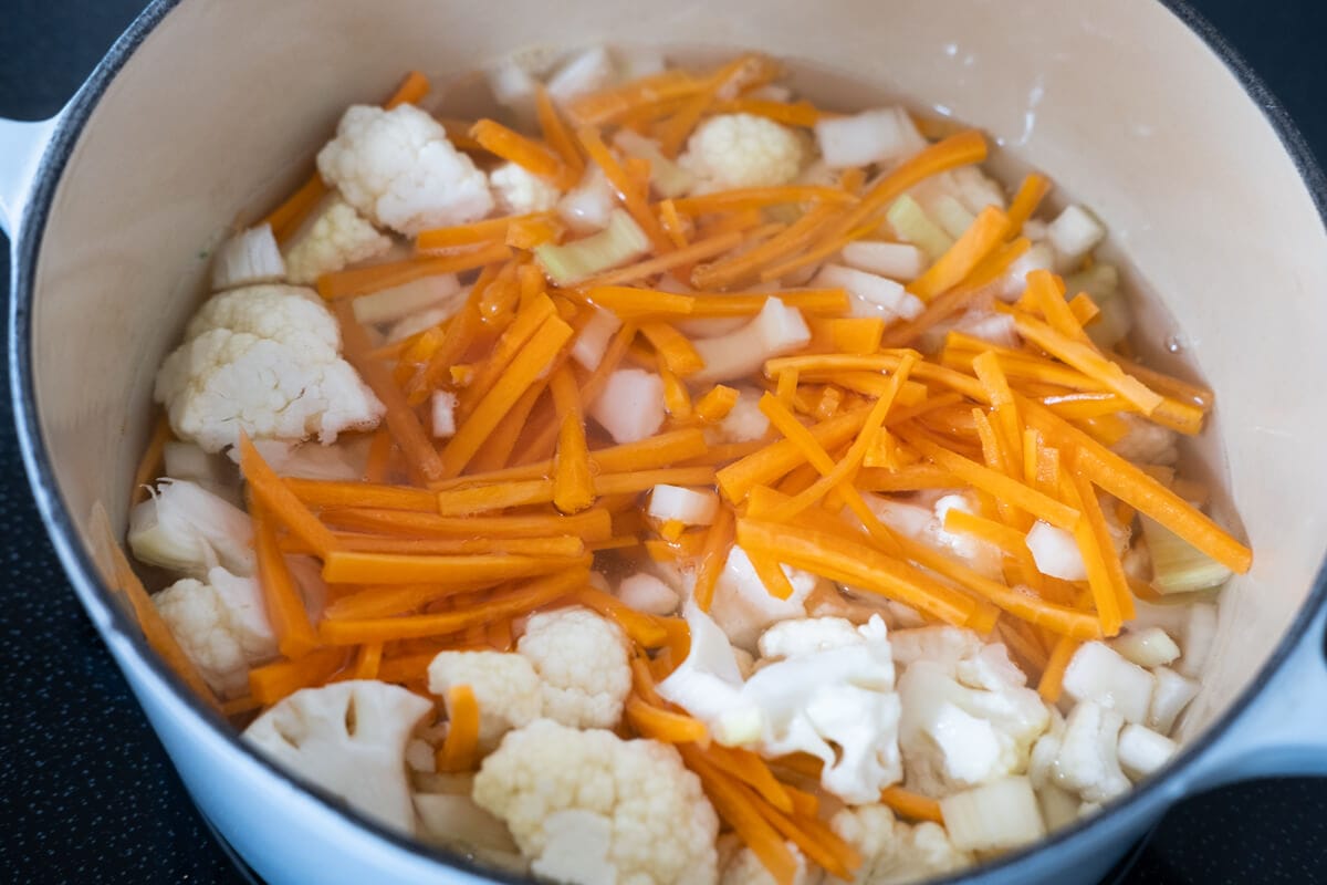 Simmer cauliflower florets, carrots, and celery in a heavy bottom pot. 