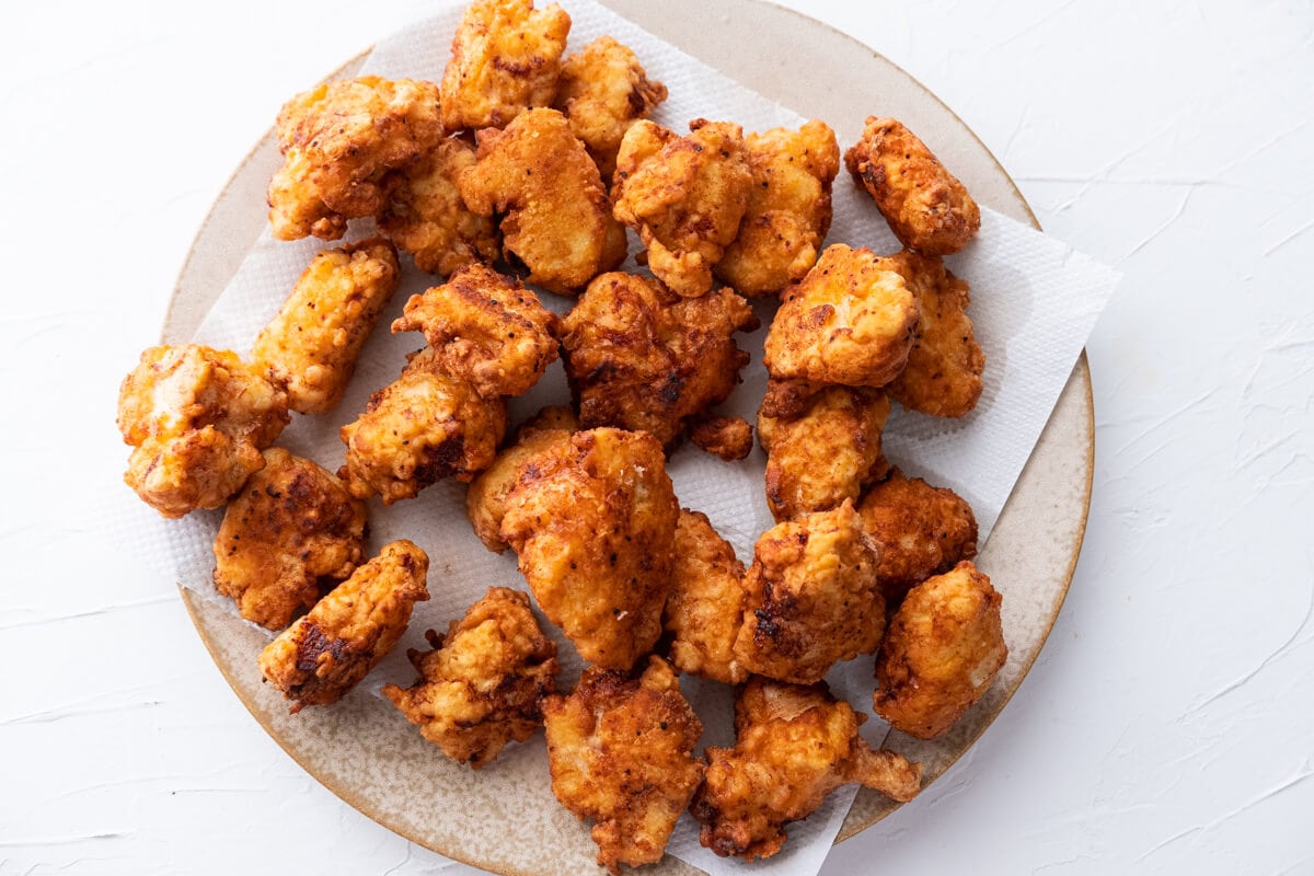 Top down picture of fresh-off-the-skillet fried chicken pieces on a plate lined with paper towel. 