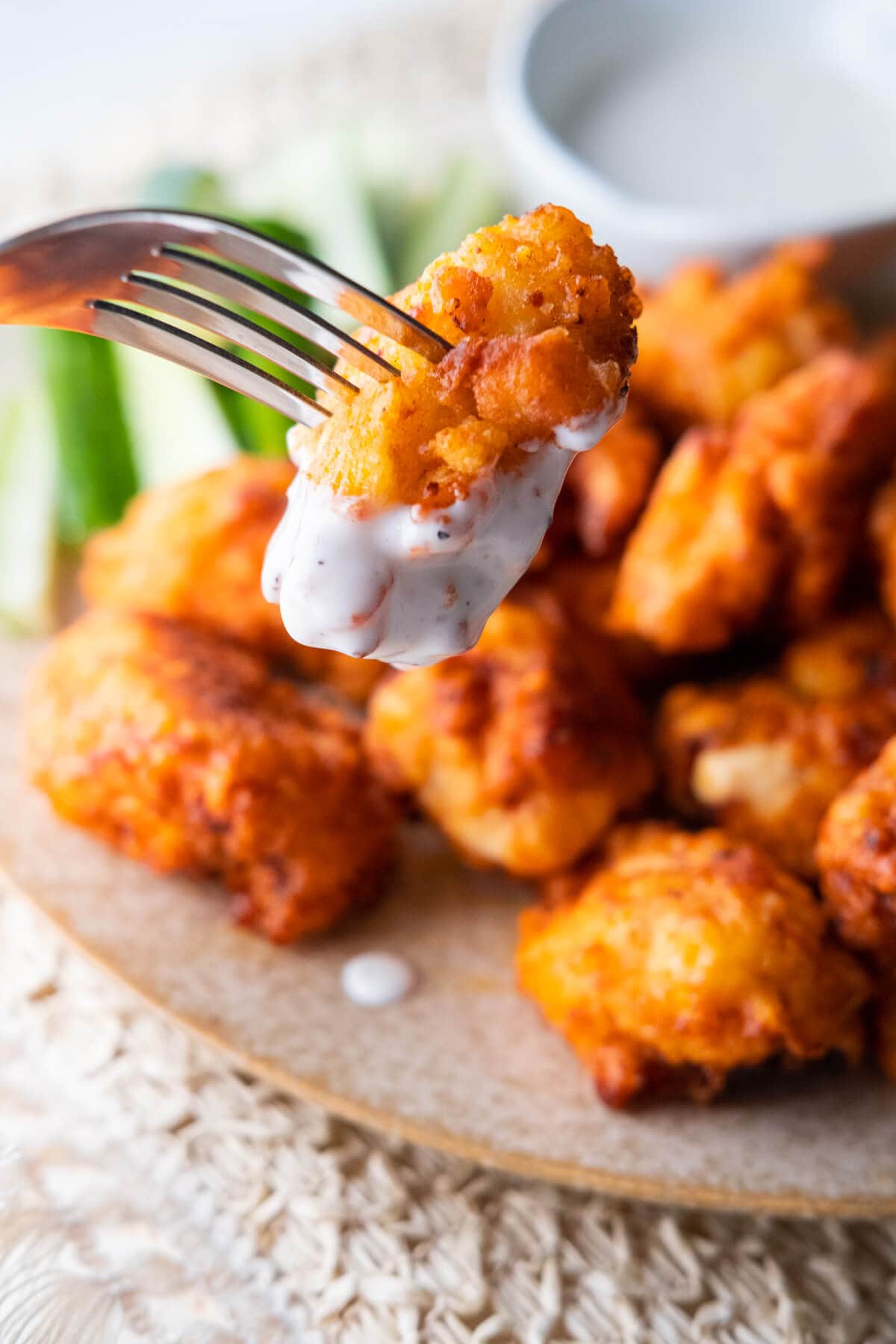 A fork poking through a piece of chicken dipped in white-color ranch dressing. 