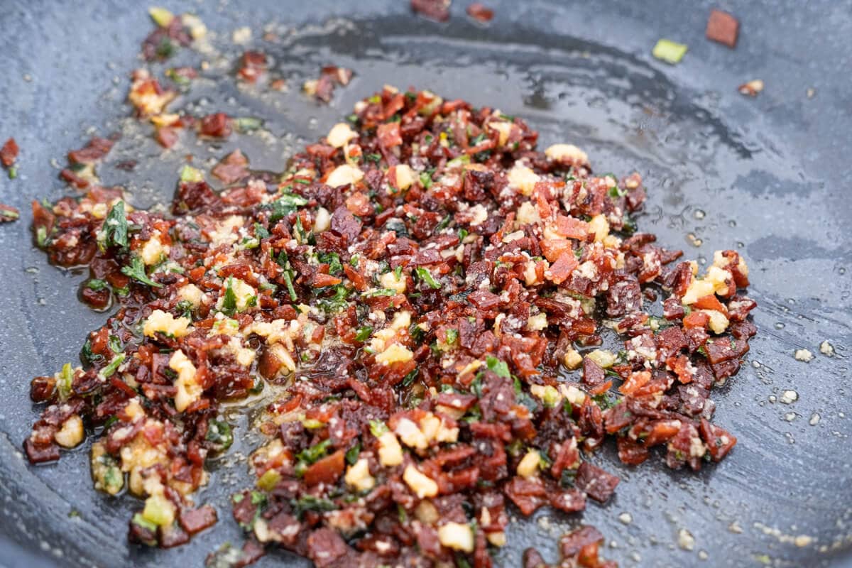 Stir-fried chopped pepperoni with garlic, parsley, green onion, and grated parmesan cheese in a frying pan. 