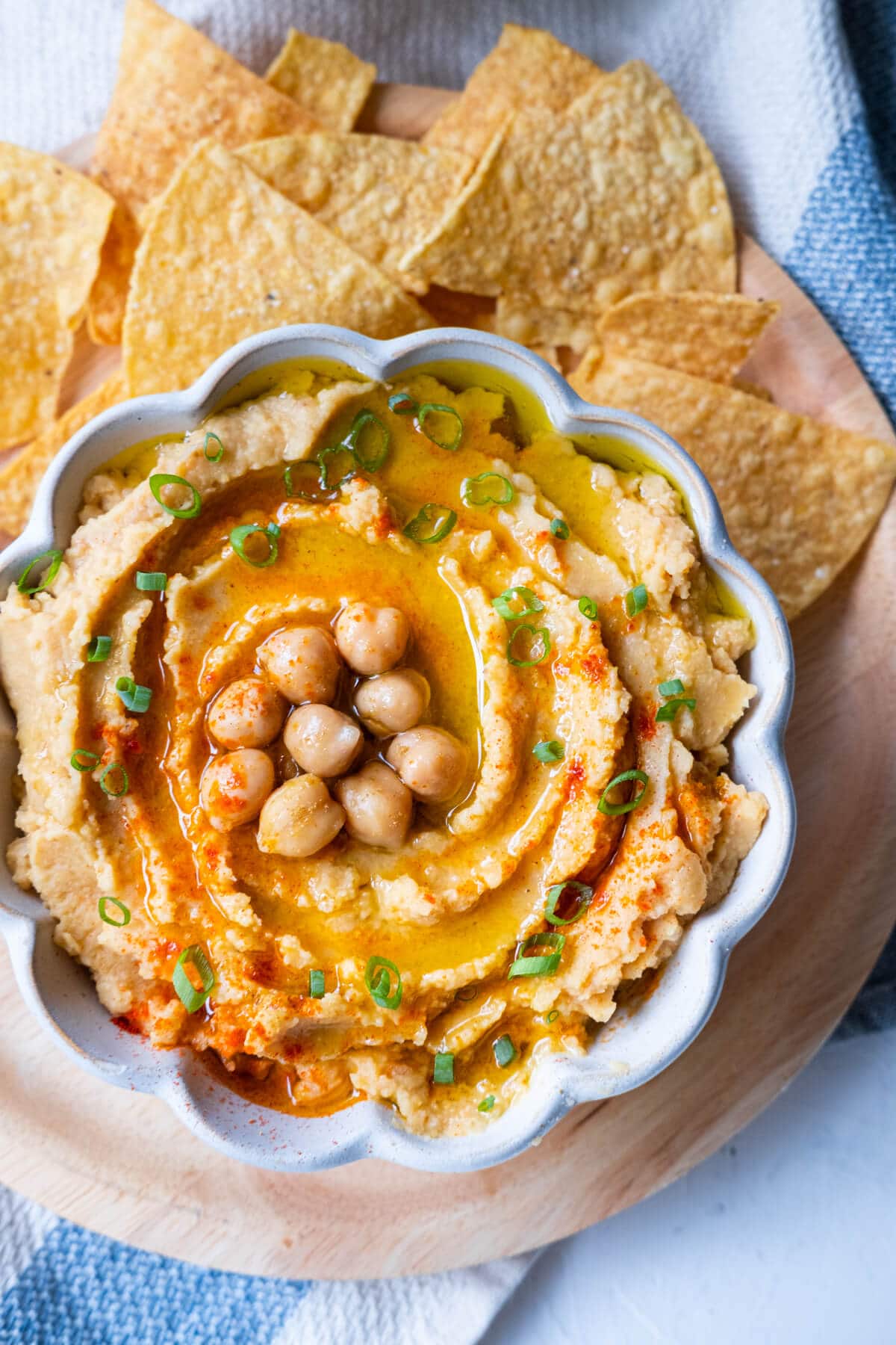Creamy hummus topped with paprika and chickpeas and drizzled with olive oil served in a bowl with nachos on the side. 