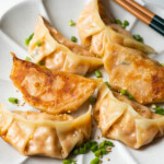 Pan-fried mandu served on a white shallow plate with scallions and white sesame seeds sprinkled on top.