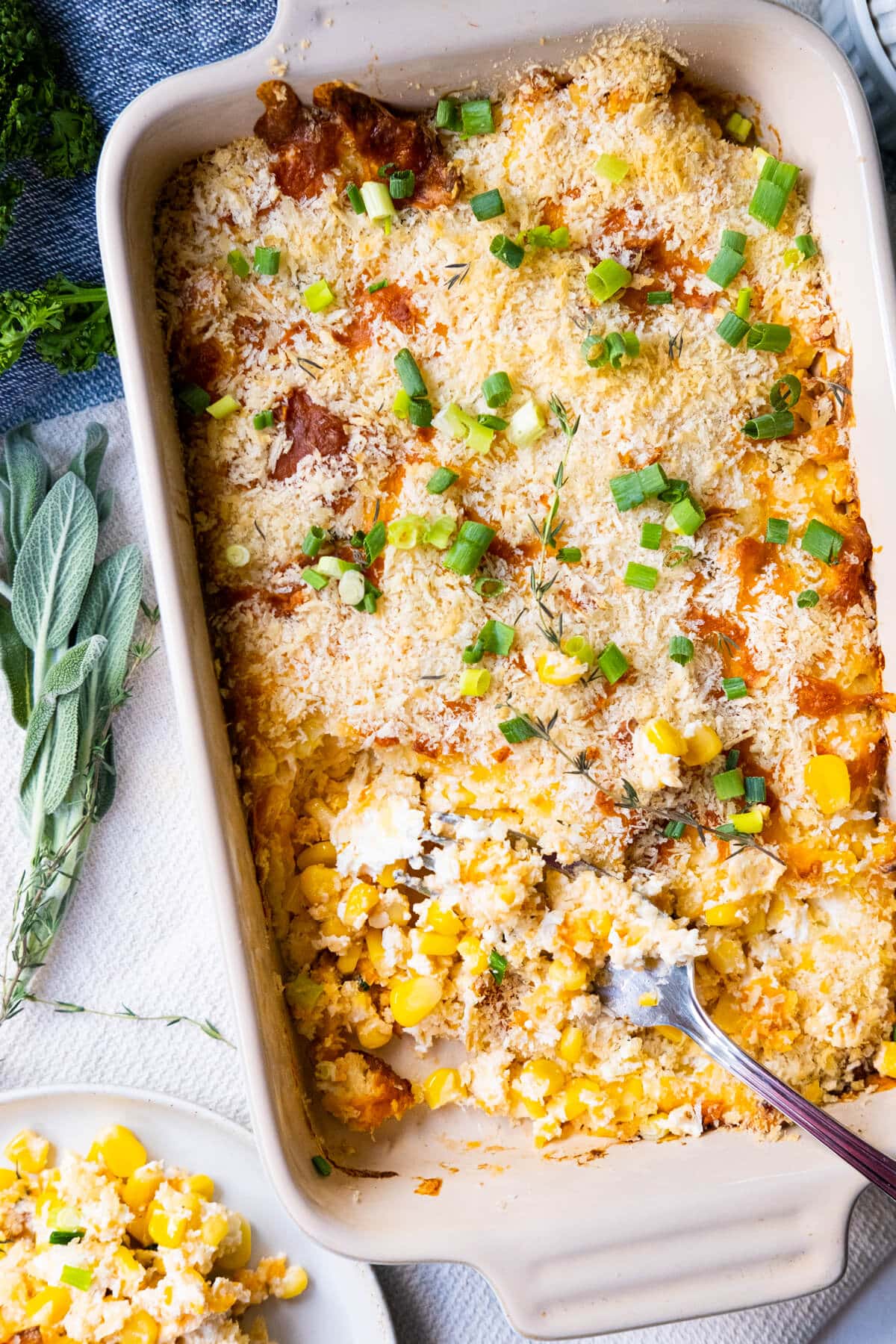 Extremely cheesy corn casserole baked in a baking dish with sage on the side. 