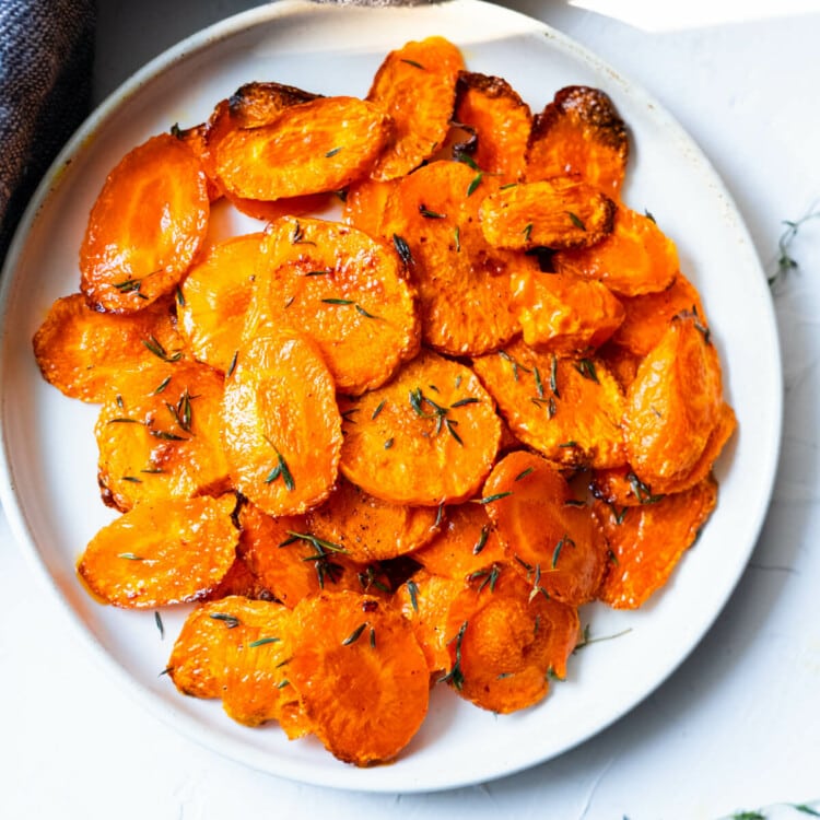Roasted carrots with thyme on top is served in a white shallow plate.
