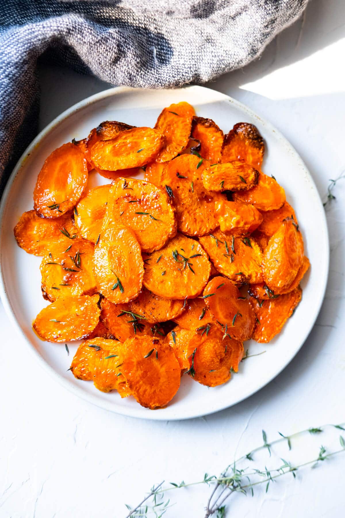 Roasted carrots with thyme on top is served in a white shallow plate.