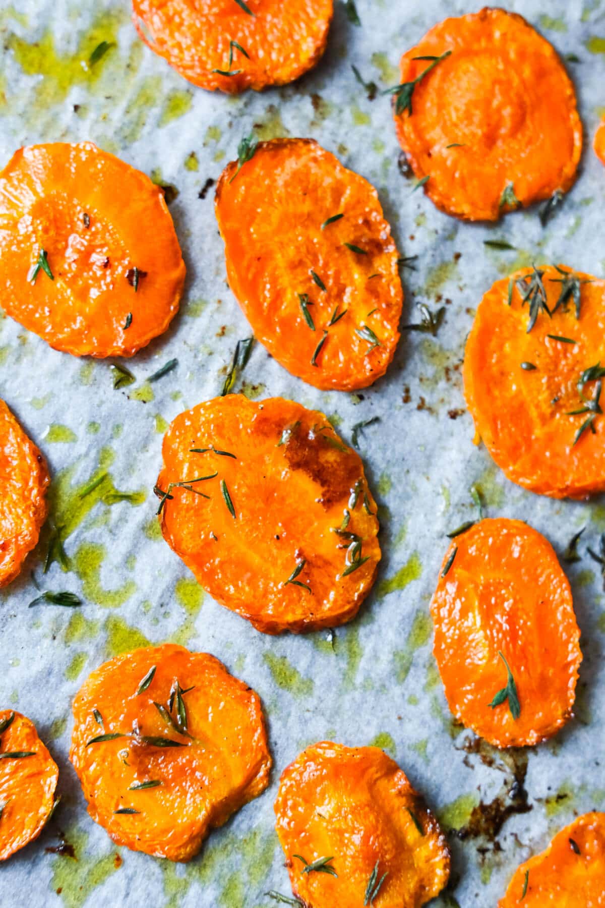 Roasted carrots with thyme on a baking pan lined with parchment paper.