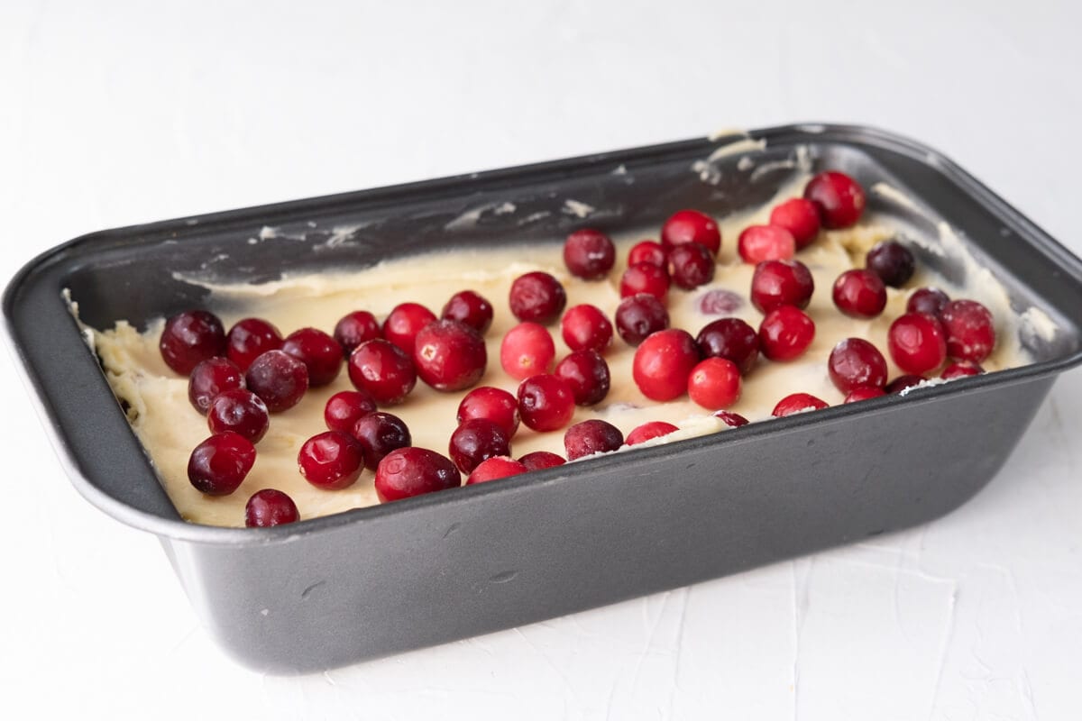 Batter topped with extra frozen cranberries transferred into a baking loaf pan. 