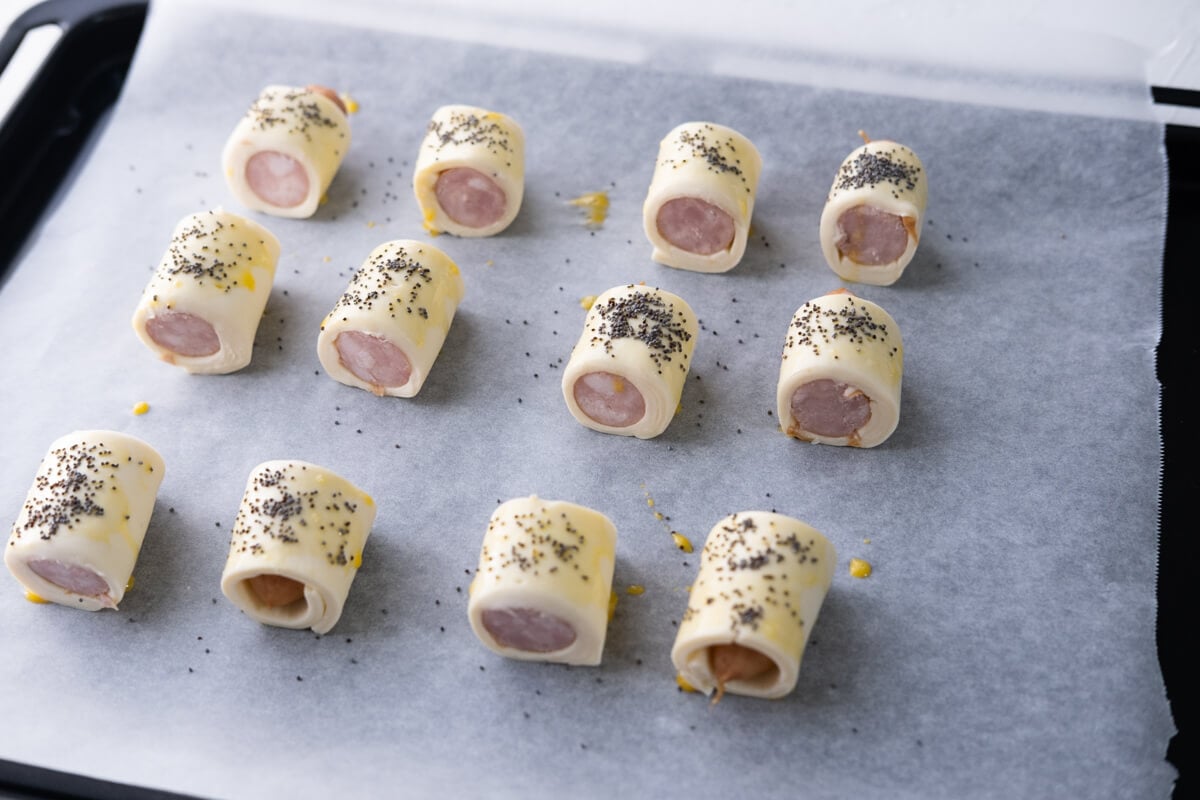 Cut the pigs in blankets in half, brush with egg wash and top with poppy seeds. 