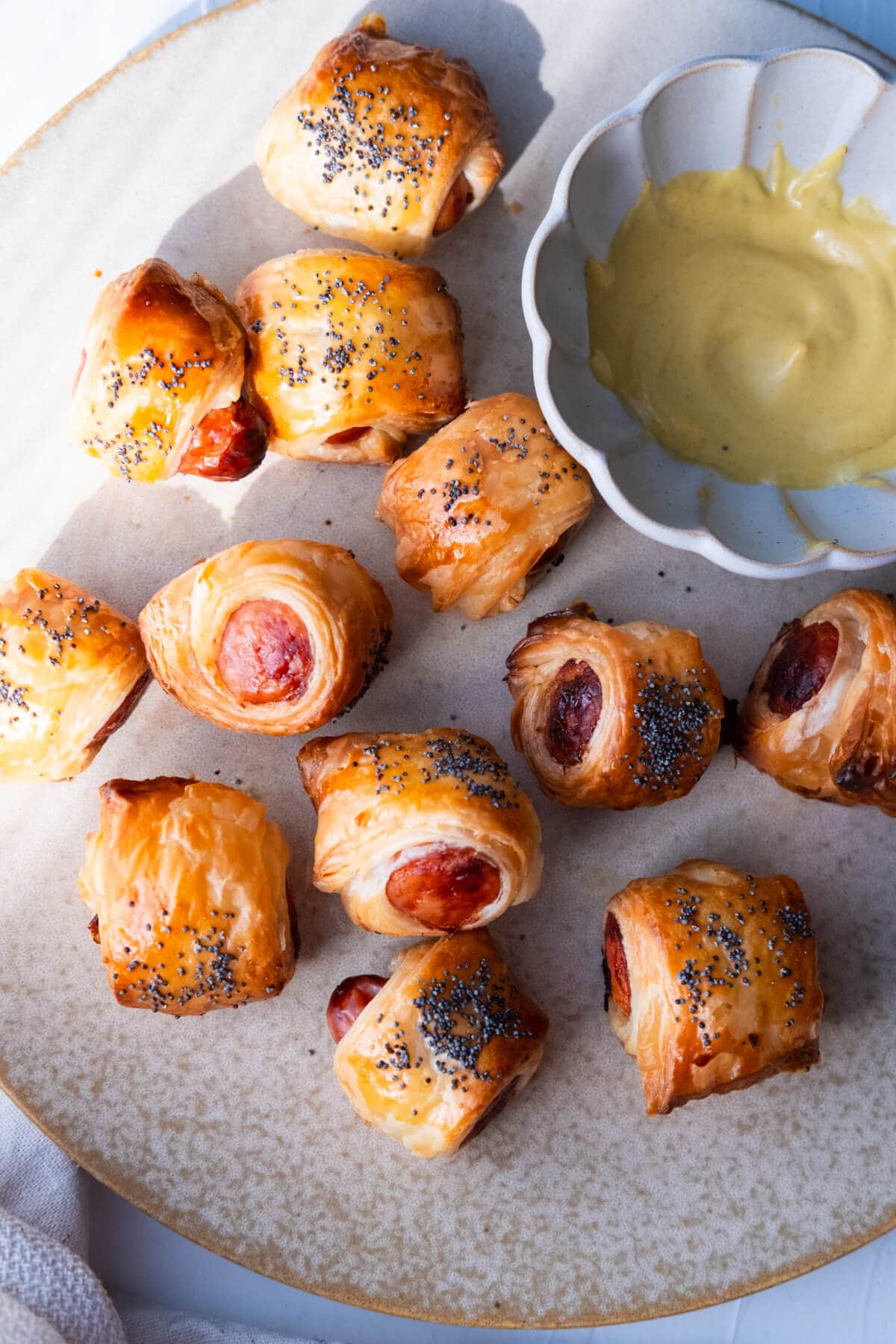 Pigs in blankets on a shallow plate and served with mustard sauce. 