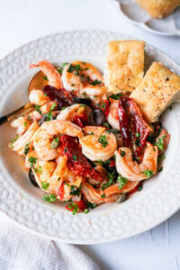 Mediterranean olive and shrimp in a shallow plate with 2 pieces of focaccia on the side.