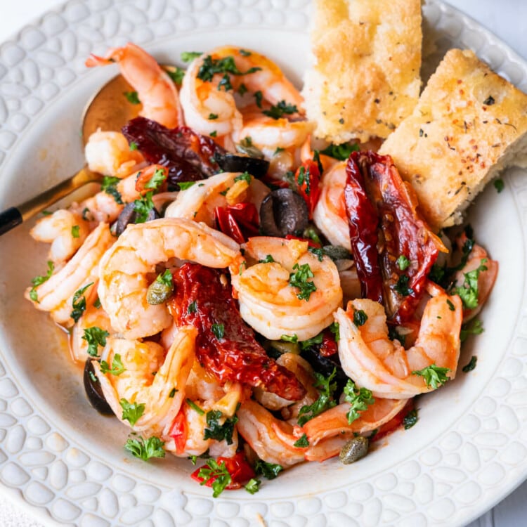 Mediterranean olive and shrimp in a shallow plate with 2 pieces of focaccia on the side.
