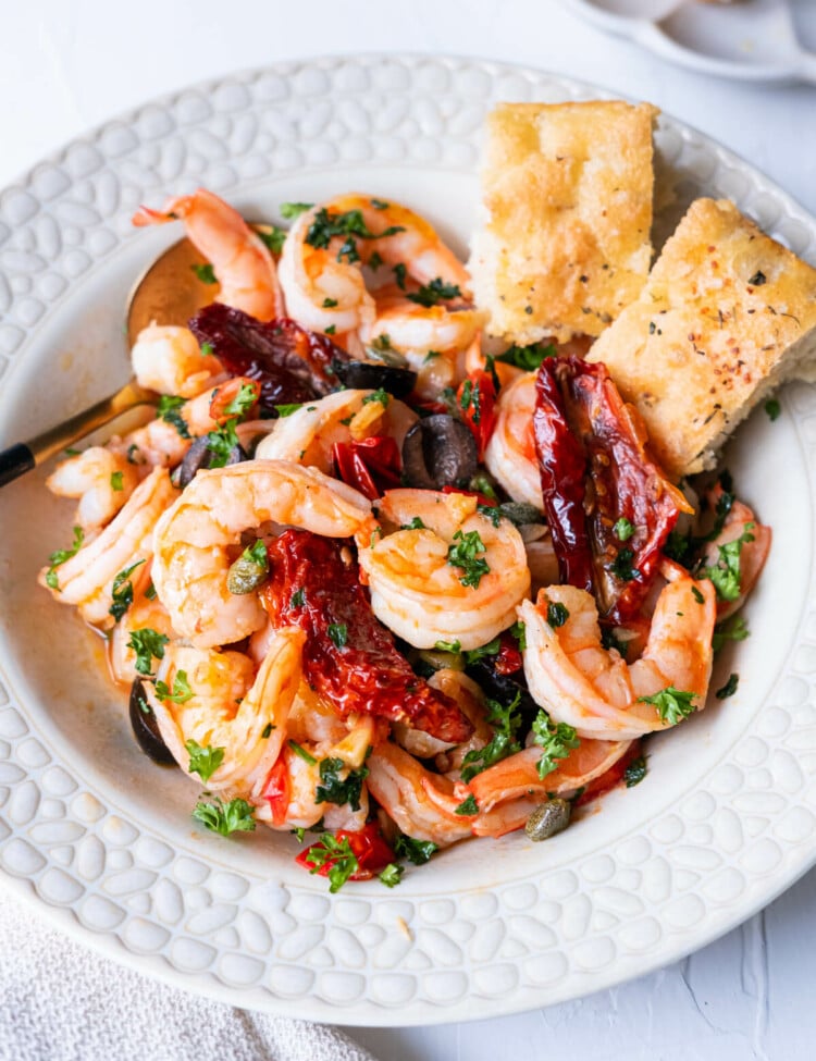 Mediterranean olive and shrimp in a shallow plate with 2 pieces of focaccia on the side.