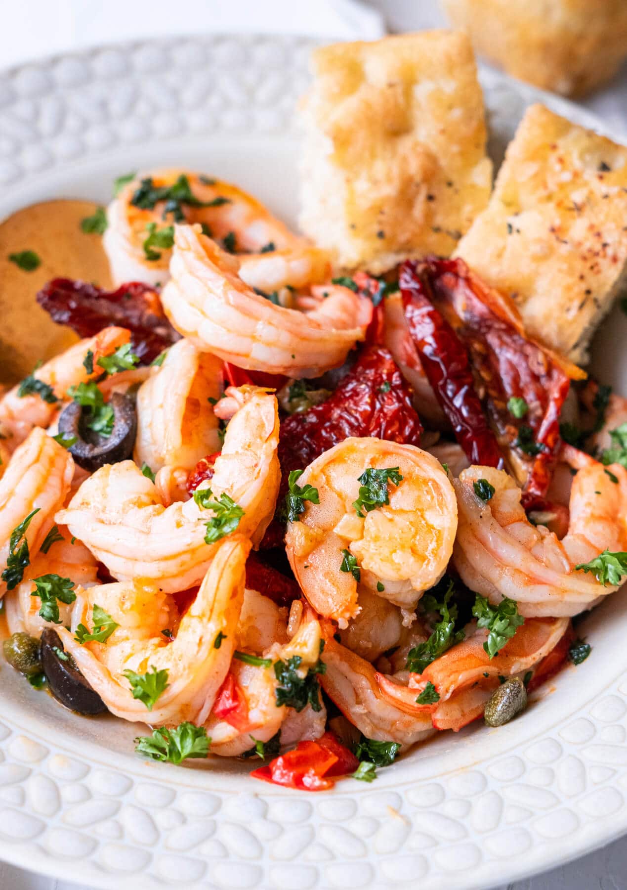 Close up of succulent shrimp with sun dried tomatoes, black olives, and freshly chopped parsley on top. 