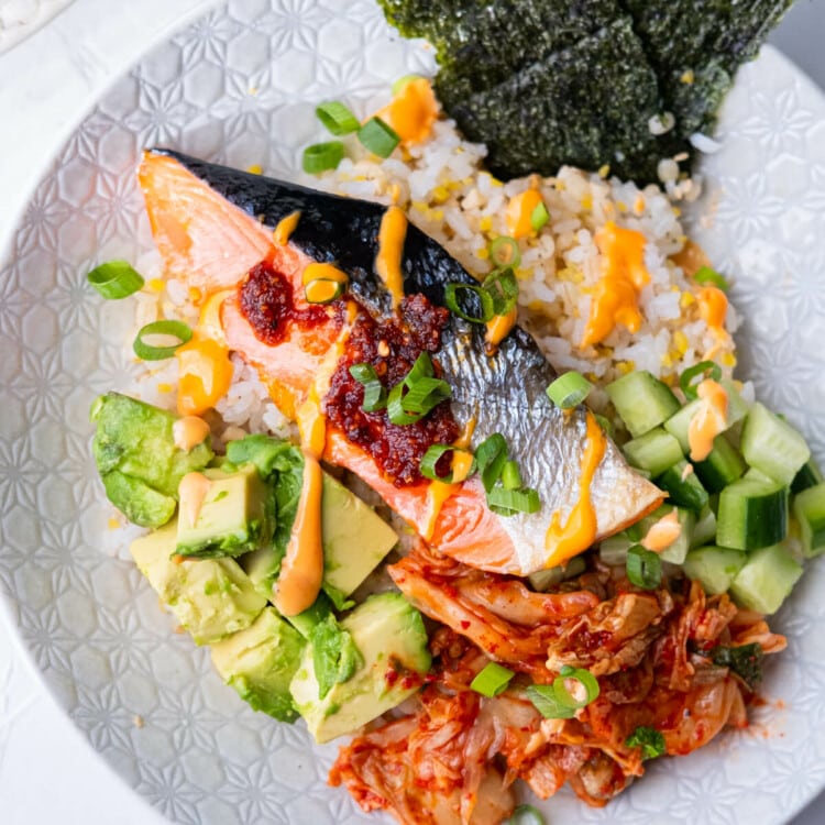 Salmon rice bowl with baked salmon, cubed avocado, cucumber, spicy kimchi, and topped with Sriracha mayo sauce and nori.