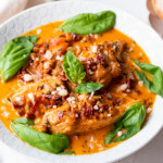 Marry me chicken with chicken breast in red creamy sauce with basil leaves on top.